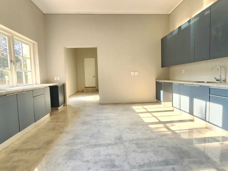A spacious, modern kitchen featuring dark blue cabinetry, stone countertops, dual sinks, and large windows, currently awaiting appliances and final finishing touches.