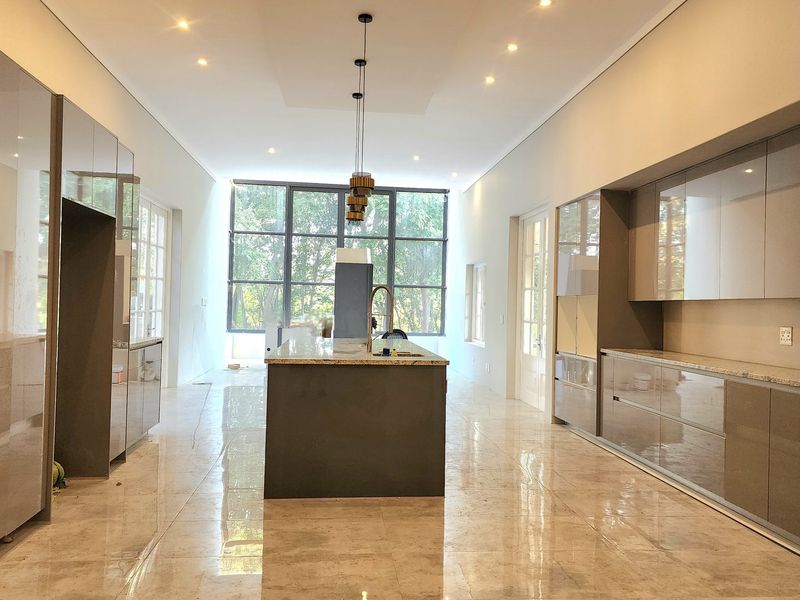 Modern open-plan kitchen featuring high-gloss cabinetry, a central island with stone countertop, recessed lighting, and large windows providing ample natural light.