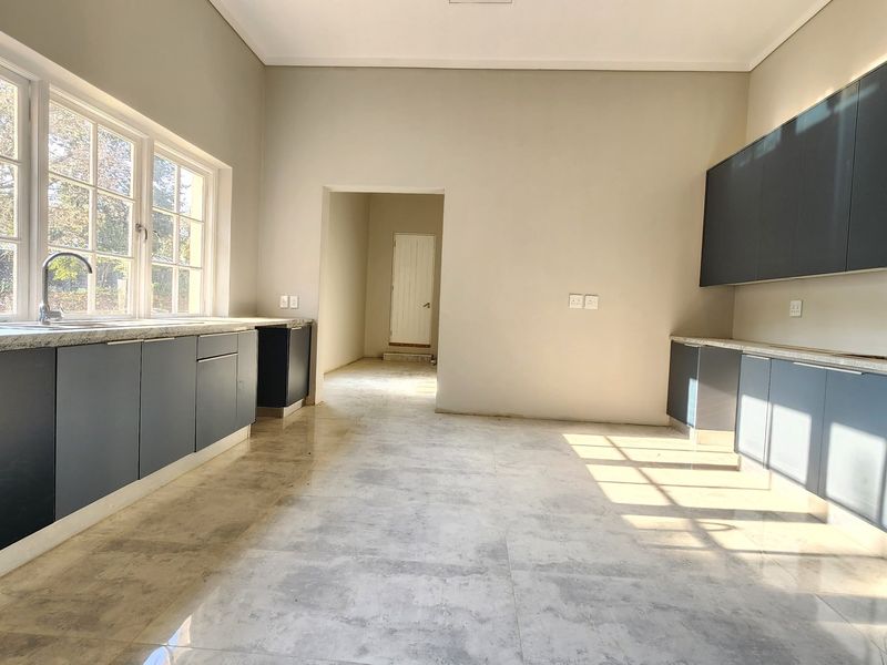 A spacious, modern kitchen featuring dark cabinetry, stone countertops, dual stainless steel sinks, and large windows providing ample natural light.