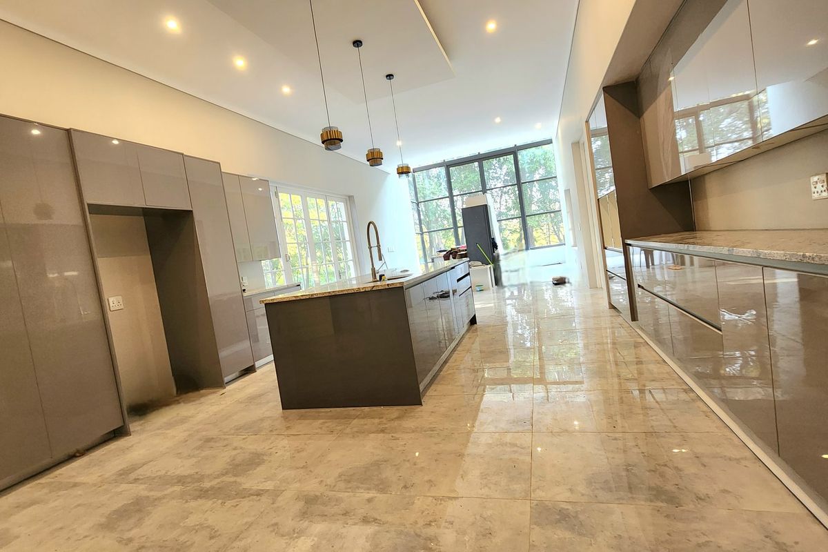 Modern open-plan kitchen featuring high-gloss cabinetry, a central island with stone countertops, recessed lighting, and large windows providing ample natural light.