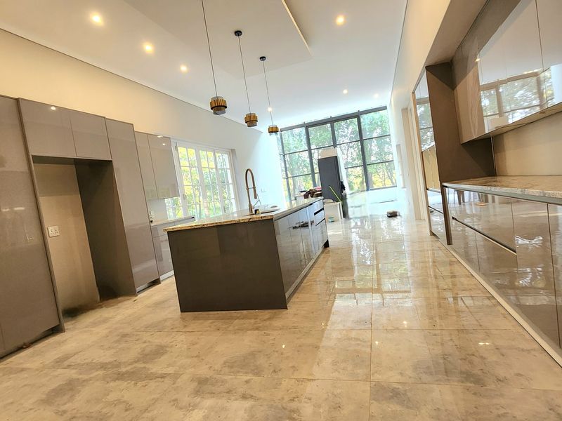 Modern open-plan kitchen featuring high-gloss cabinetry, a central island with stone countertops, recessed lighting, and large windows providing ample natural light.