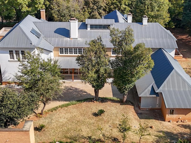 Aerial view of a large residential property featuring a multi-pitched corrugated metal roof, brick and rendered facade, and expansive surrounding garden grounds.