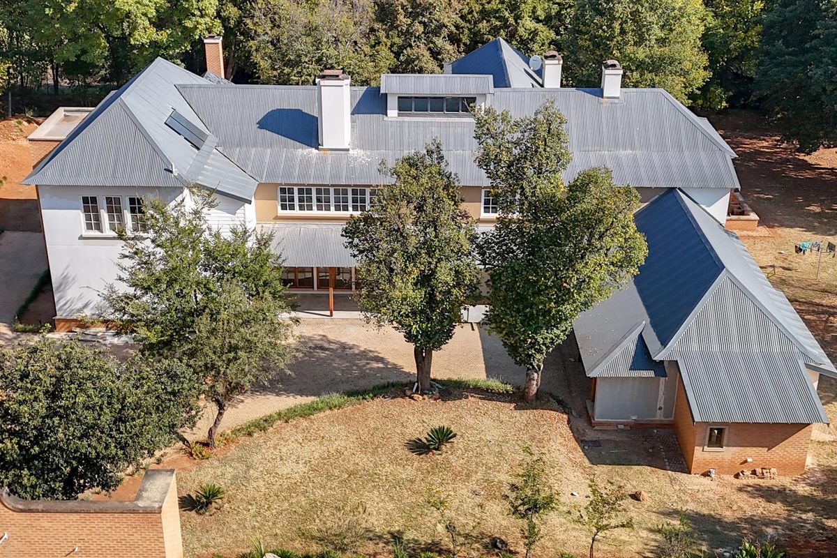 Aerial view of a large residential property featuring a multi-pitched corrugated metal roof, brick and rendered facade, and expansive surrounding garden grounds.