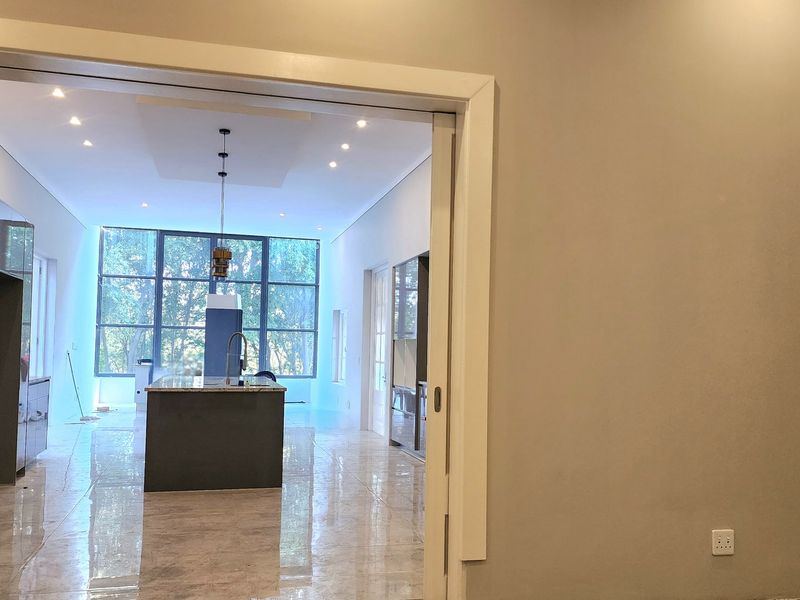 A view through a doorway into a modern open-plan kitchen featuring a central island, sleek cabinetry, and large floor-to-ceiling windows.