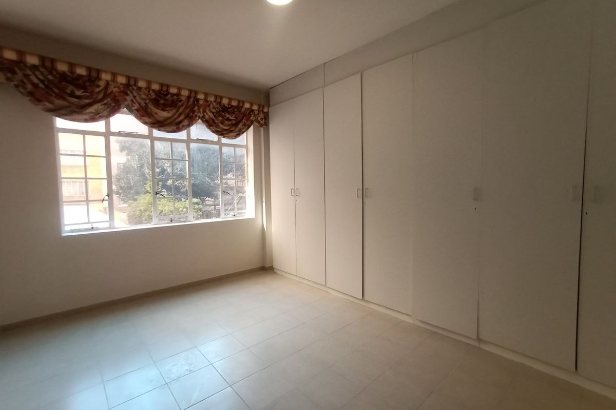 A bright, empty bedroom featuring neutral tiled flooring and extensive built-in cupboard storage, offering a clean canvas for personalization.