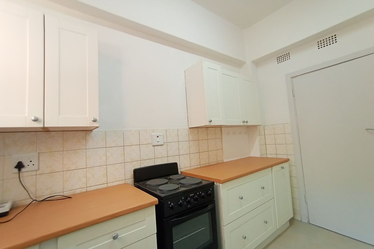 A clean, functional kitchen featuring white cabinetry, laminate countertops, tiled backsplash, and a freestanding electric stove.