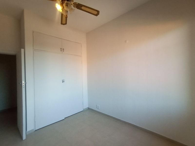 An empty bedroom featuring neutral tiled flooring, a built-in wardrobe with overhead storage, and a ceiling fan.