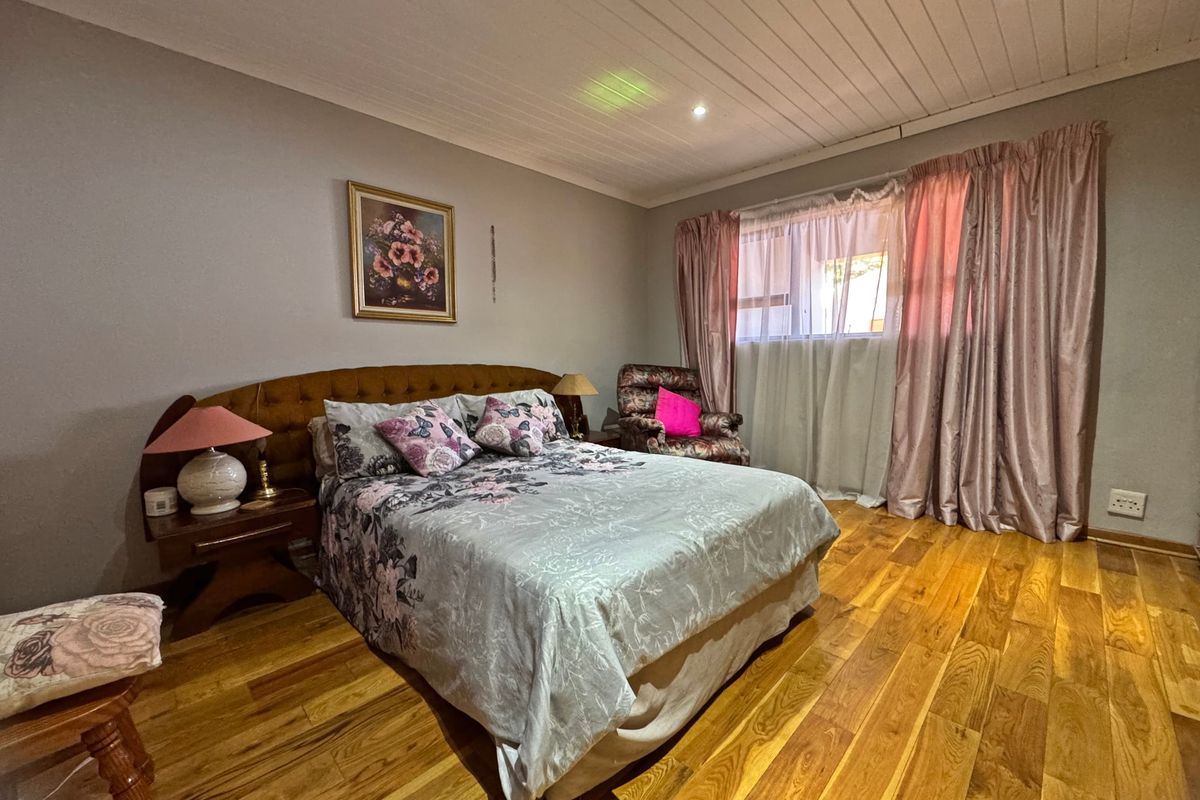 A spacious bedroom featuring warm timber flooring, a classic tongue and groove ceiling, and recessed downlighting, offering a comfortable and well-maintained living space.