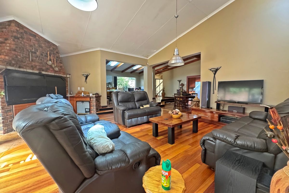 Spacious living room featuring vaulted ceilings, hardwood flooring, and a prominent exposed brick fireplace, offering a warm and inviting atmosphere.