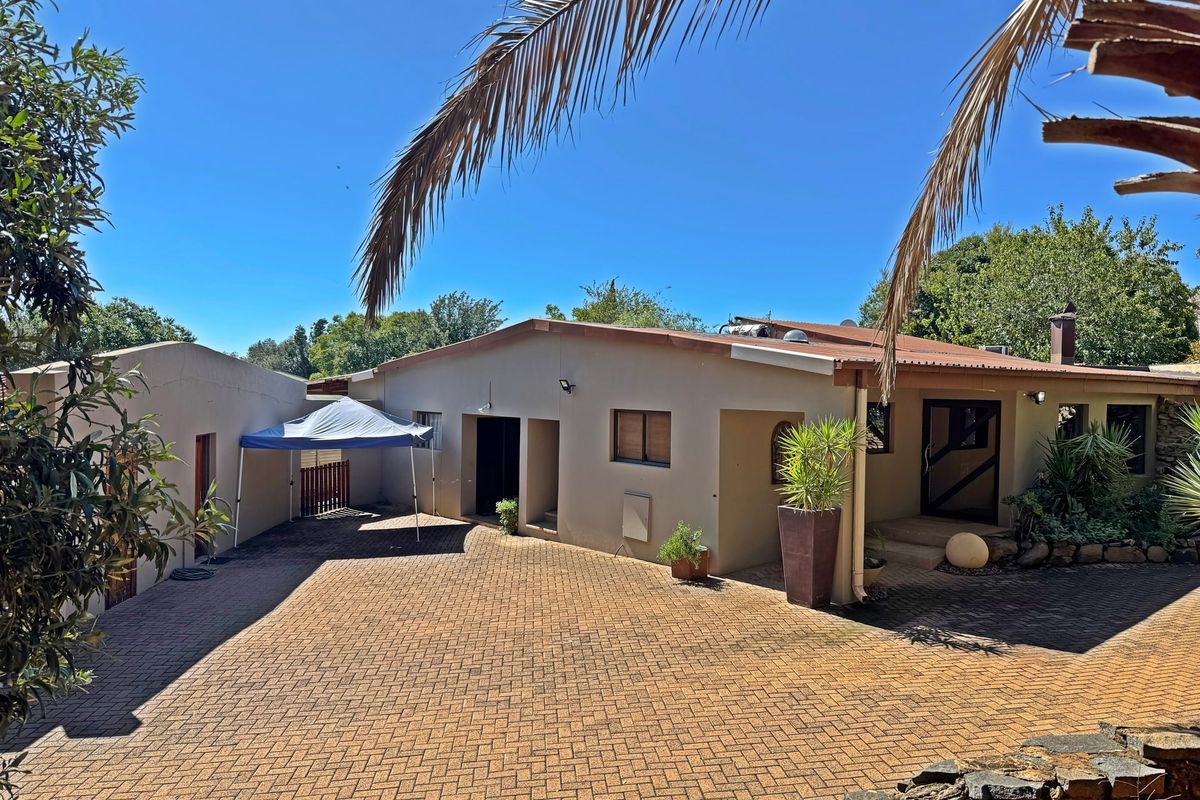 Rear exterior view of the property featuring a large paved courtyard area and a single-story structure with a corrugated metal roof.