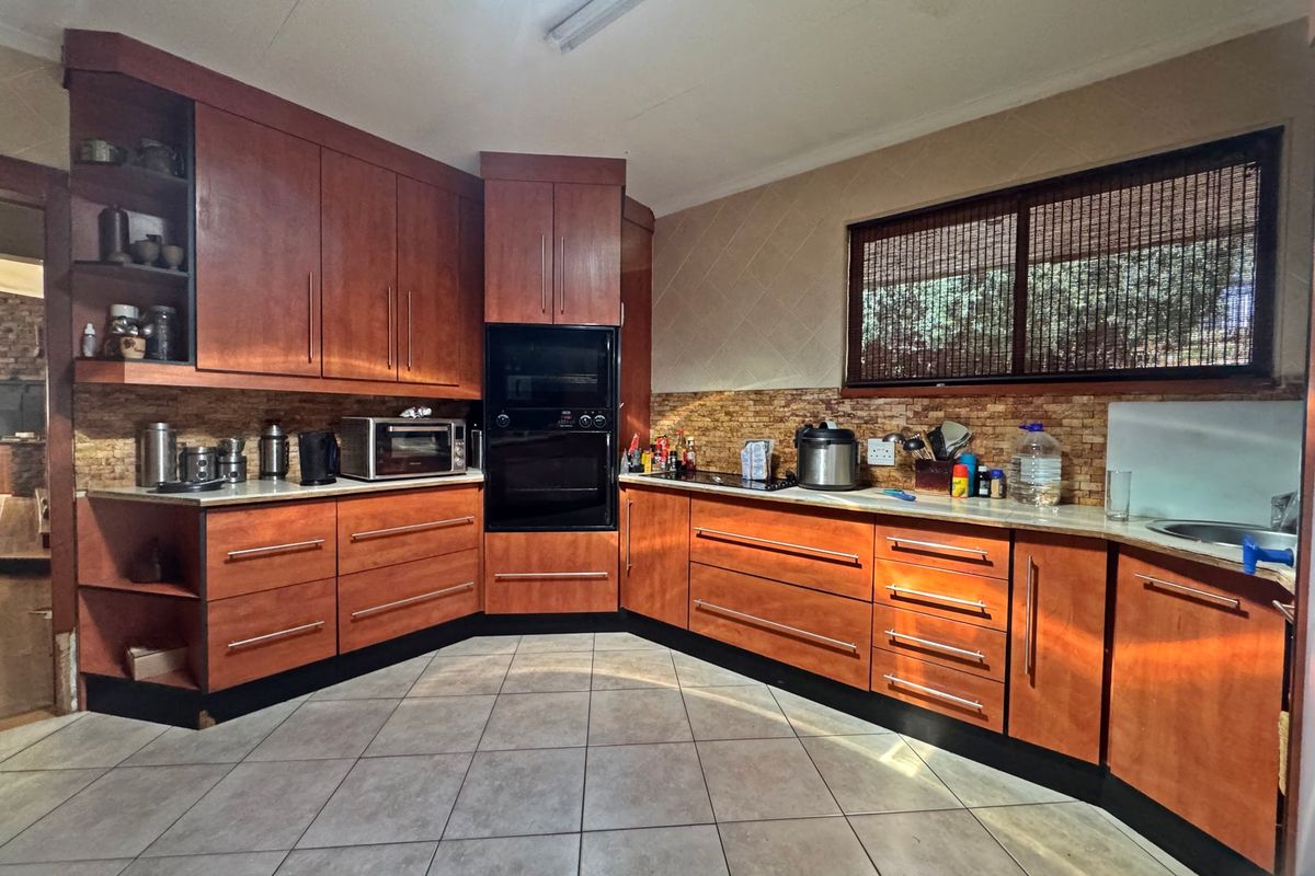 A functional kitchen featuring warm-toned wooden cabinetry, built-in oven, hob, stone-look backsplash, and tiled flooring with ample counter space.