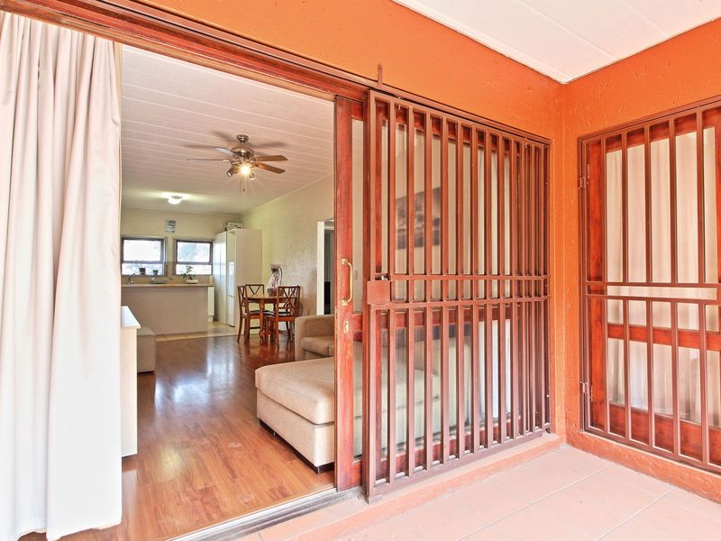 Covered patio area featuring a sliding security gate and access to the interior living space, finished with tiled flooring.