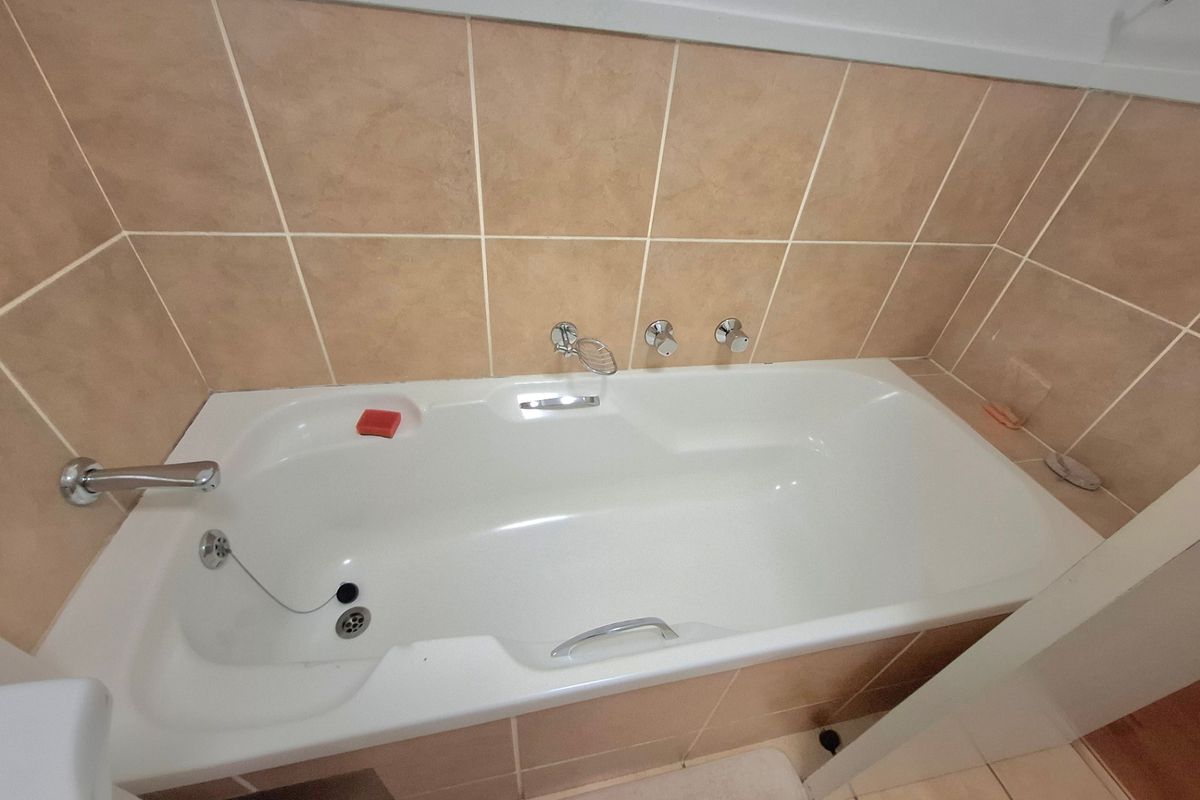 A clean bathroom featuring a built-in bathtub with chrome fixtures and neutral ceramic wall tiling.