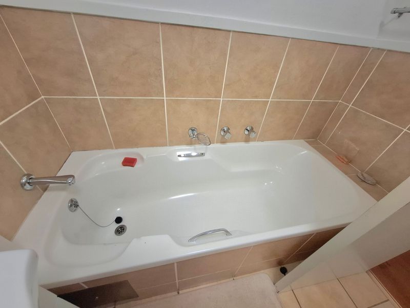 A clean bathroom featuring a built-in bathtub with chrome fixtures and neutral ceramic wall tiling.