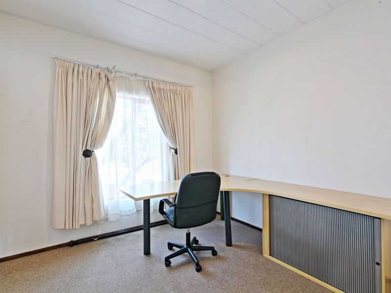 A functional home office space featuring neutral carpet flooring, a built-in desk unit, and window treatments.