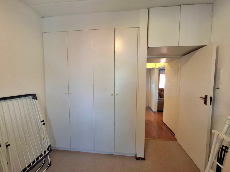 A bedroom featuring built-in cupboards with overhead storage and neutral carpet flooring, offering a functional space with potential for modernization.