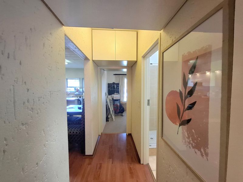 A functional hallway featuring laminate flooring, textured walls, and a built-in overhead storage cabinet, providing access to adjacent living and bathroom areas.