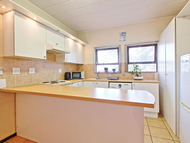 Functional kitchen featuring laminate countertops, built-in cabinetry, electric hob, extractor fan, and tiled backsplash with integrated laundry plumbing.