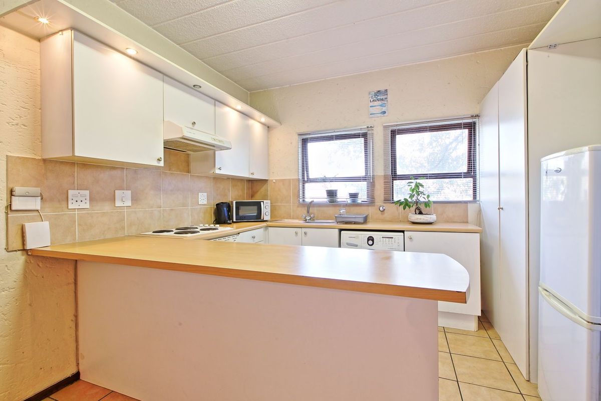 Functional kitchen featuring laminate countertops, built-in cabinetry, electric hob, extractor fan, and tiled backsplash with integrated laundry plumbing.