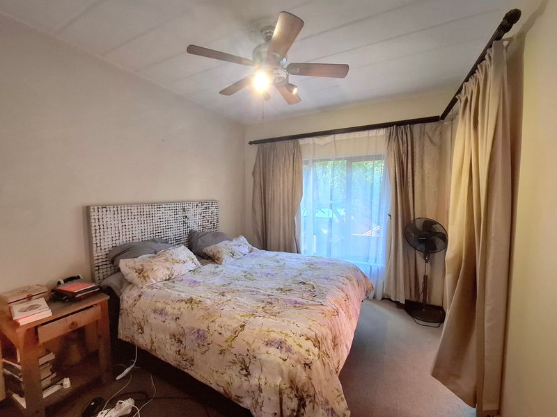 A functional bedroom featuring a ceiling fan, carpeted flooring, and large window with curtain rods, providing a comfortable and well-lit sleeping space.