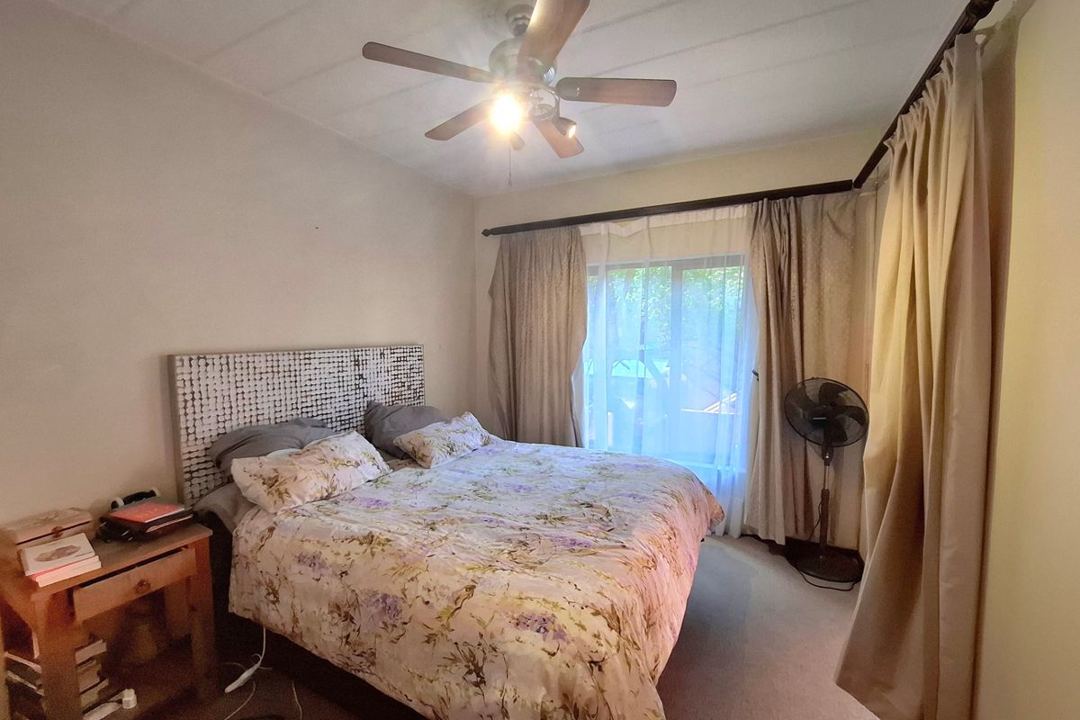 A functional bedroom featuring a ceiling fan, carpeted flooring, and large window with curtain rods, providing a comfortable and well-lit sleeping space.