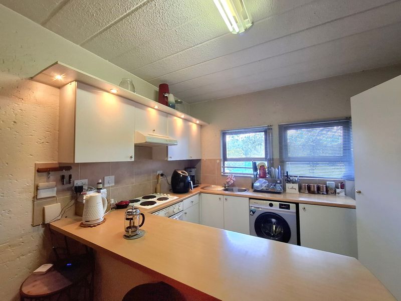 Functional kitchen featuring built-in cabinetry, laminate countertops, an electric hob, and an integrated washing machine with a breakfast bar area.