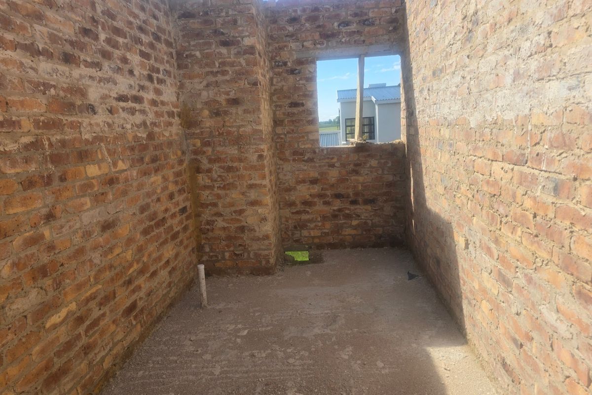 An unfinished room under construction featuring exposed brick walls, a concrete floor, and a window opening.