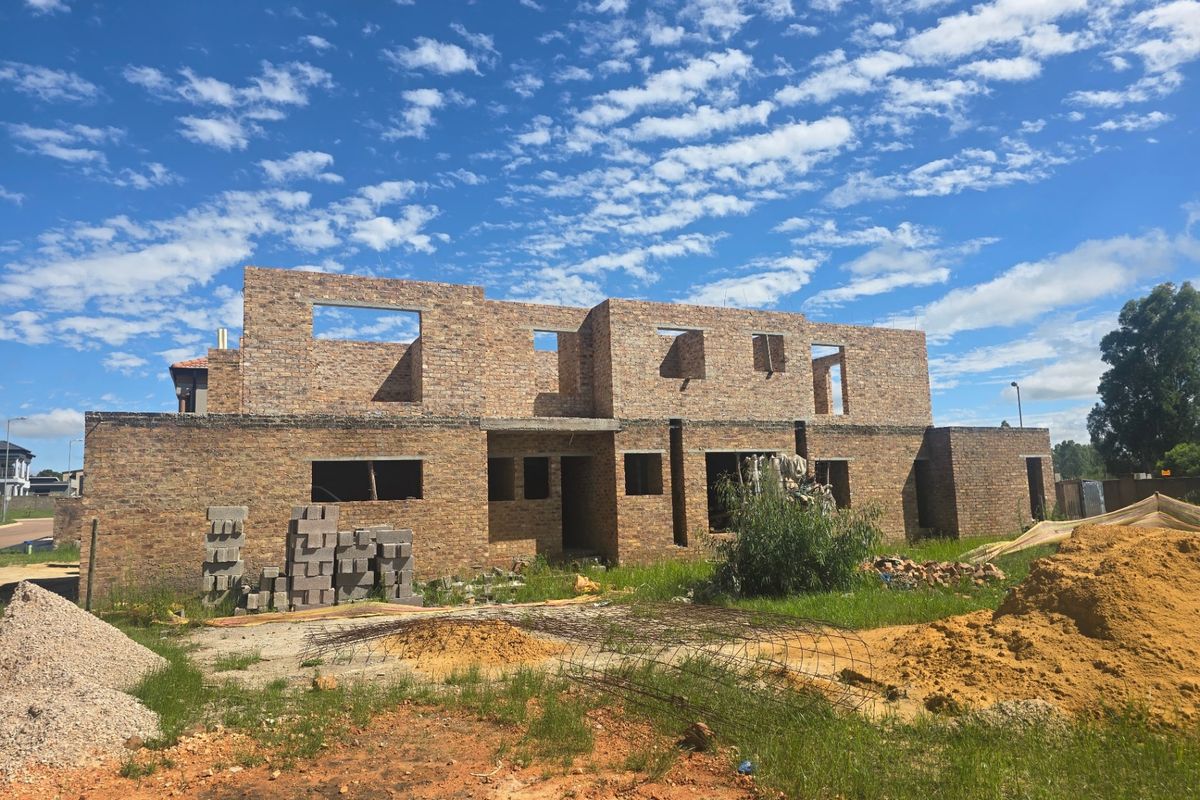 A rear view of a residential property currently under construction, featuring a face brick structure with open window frames and an unfinished site.