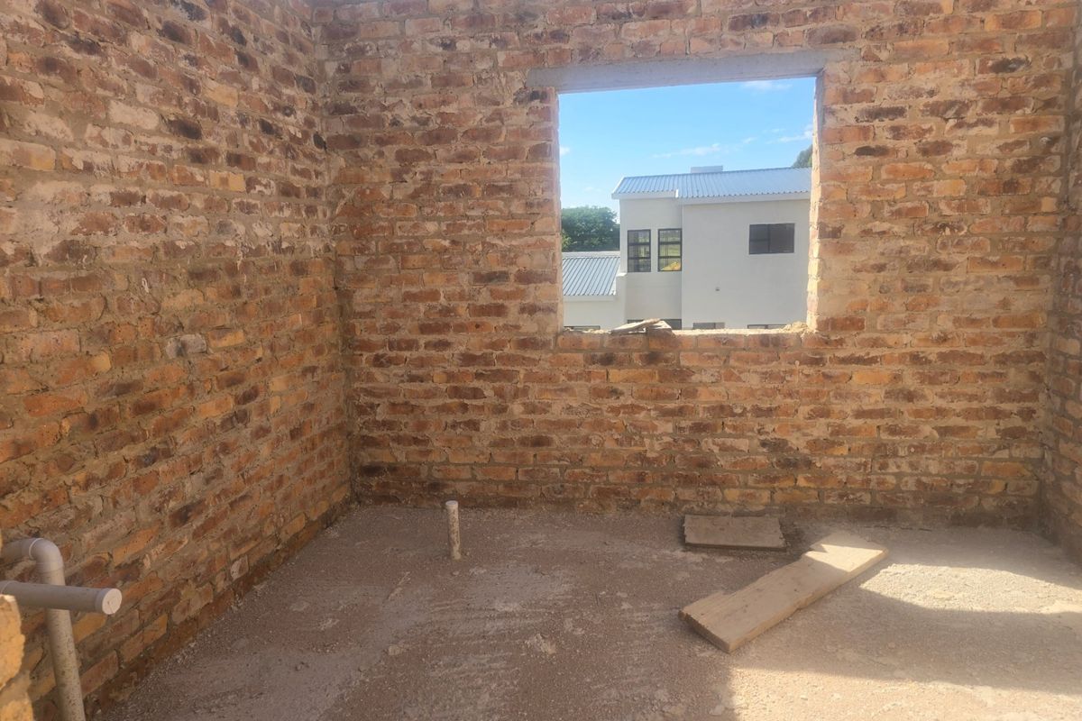 An unfinished room under construction featuring exposed brick walls and plumbing rough-ins, awaiting final finishes and fixtures.
