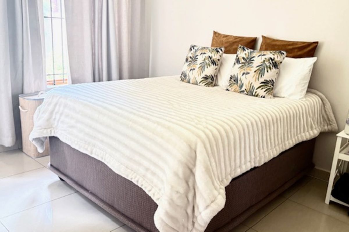 A bright and well-maintained bedroom featuring tiled flooring and large windows with curtains, providing a clean and comfortable living space.