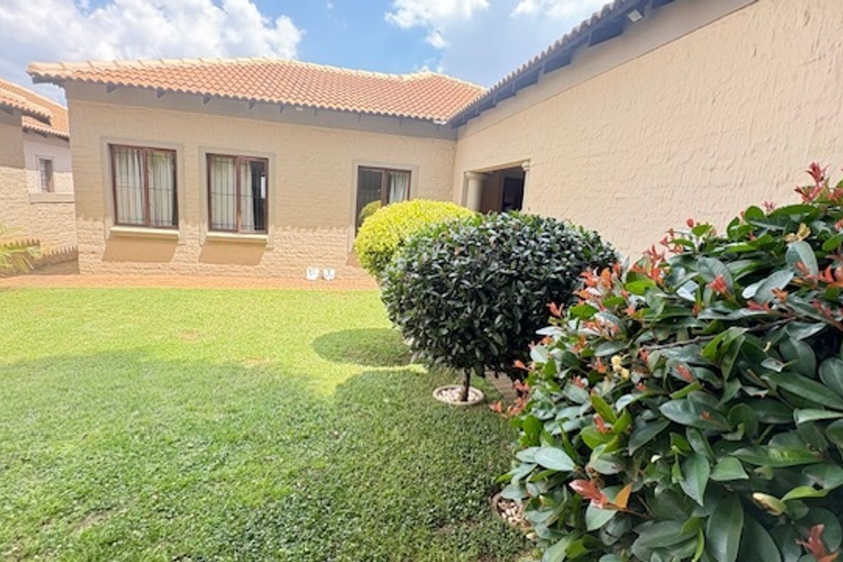 A well-maintained rear garden area featuring a manicured lawn and established shrubs, set against the exterior wall of the cluster home.