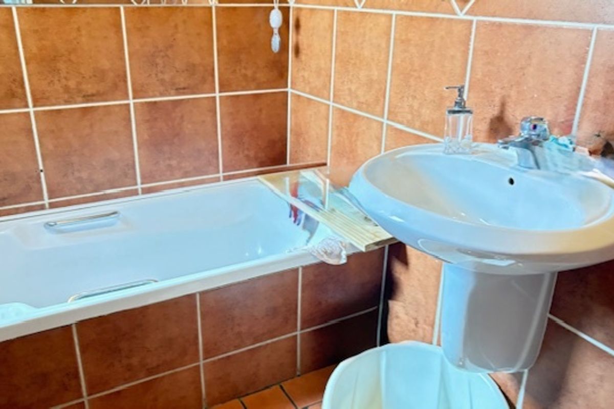 A functional bathroom featuring a standard bathtub and a pedestal basin with terracotta-style wall tiling.