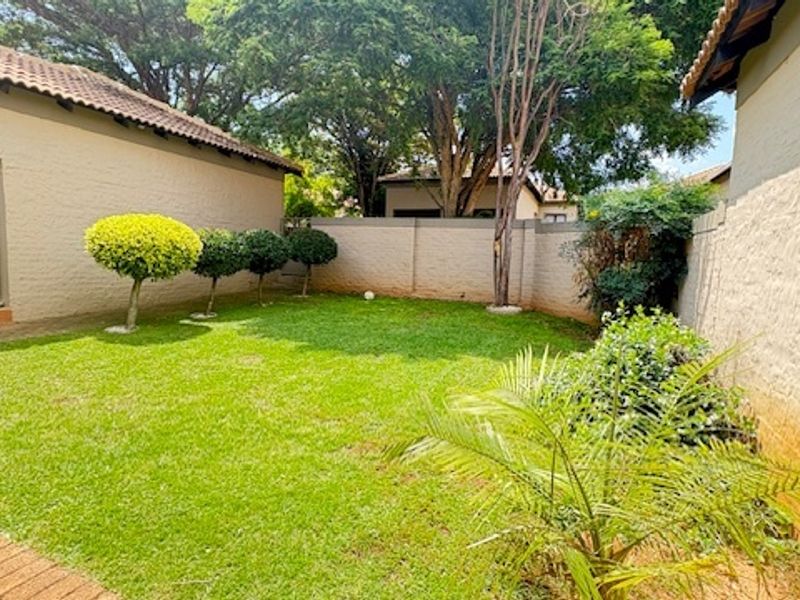 A private rear garden area featuring a well-maintained lawn, perimeter boundary walls, and a paved walkway leading to the main dwelling structure.