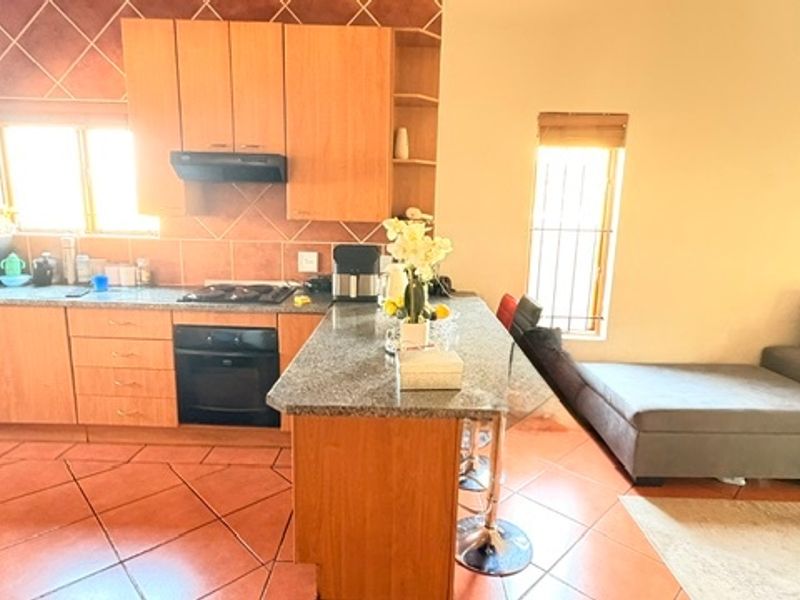 Open-plan kitchen and living area featuring wooden cabinetry, granite countertops, built-in oven, gas hob, and tiled flooring throughout.