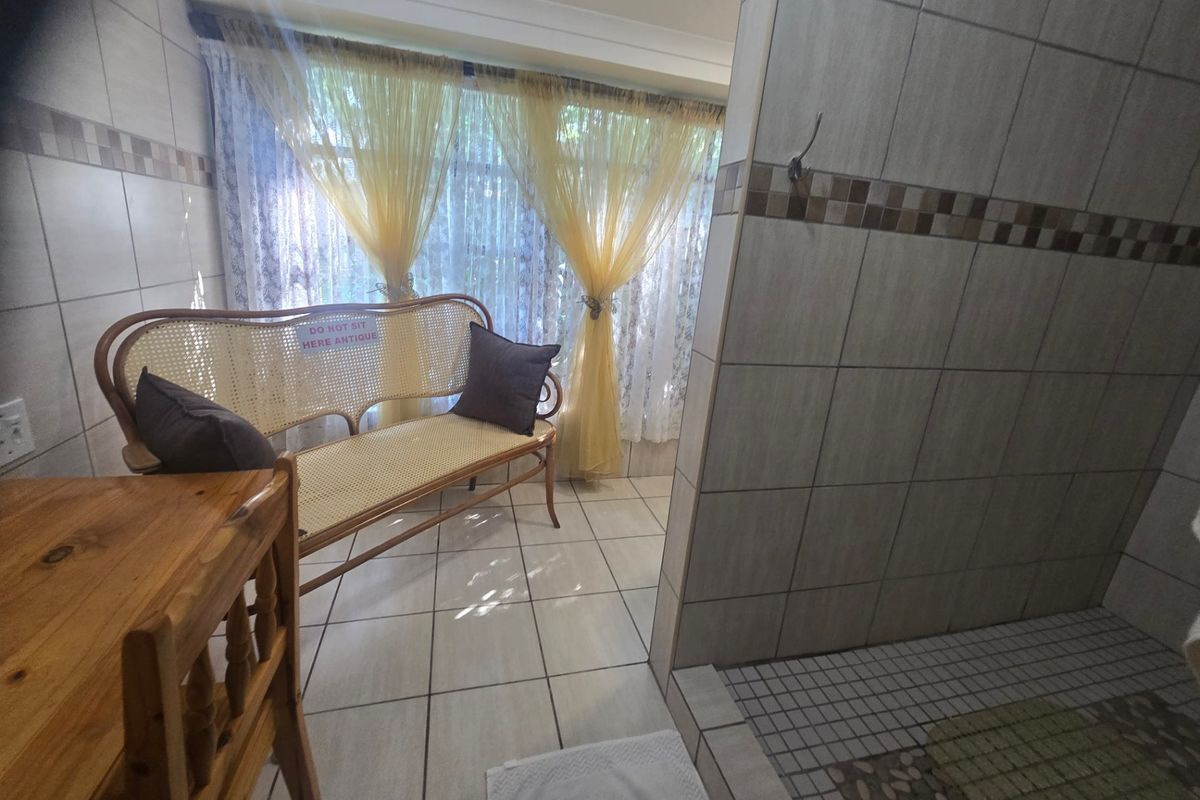 A bathroom featuring tiled walls with a decorative border and a shower area, currently styled with seating.