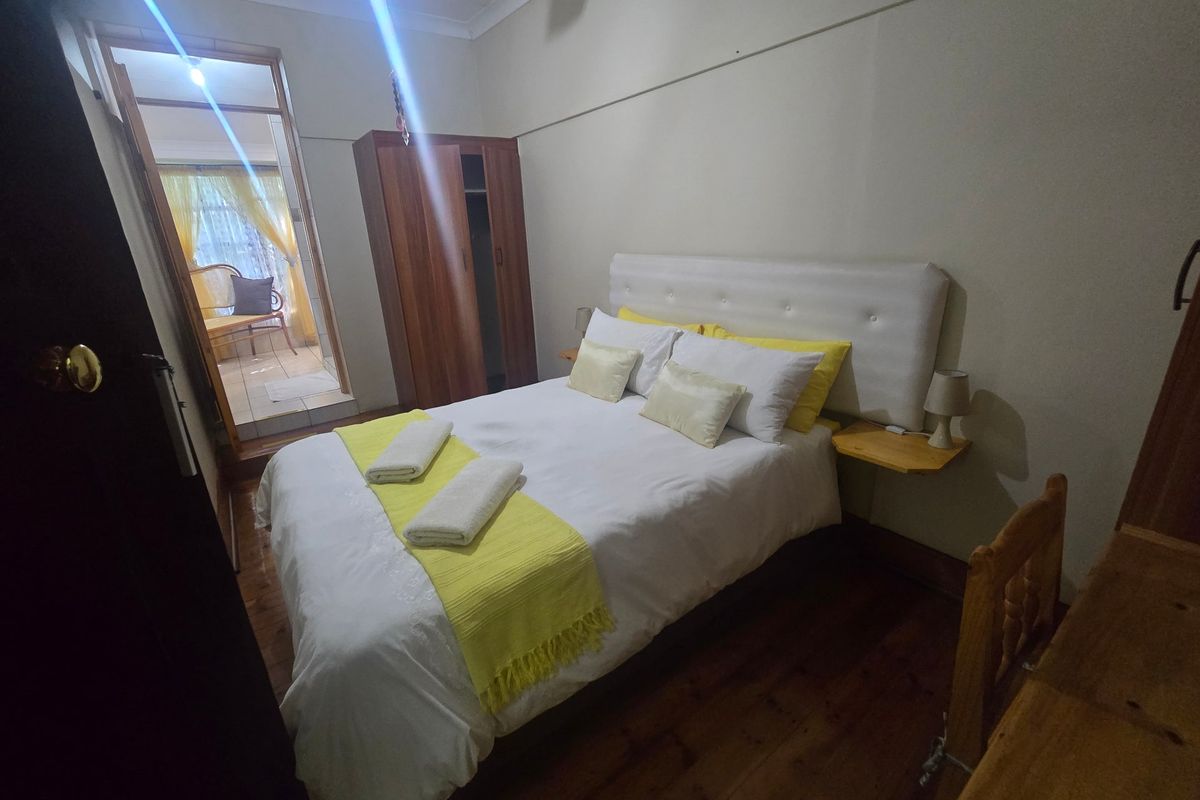 A bedroom featuring polished timber flooring, a built-in wardrobe, and coved ceilings, with an adjoining sunroom or patio area visible through the doorway.