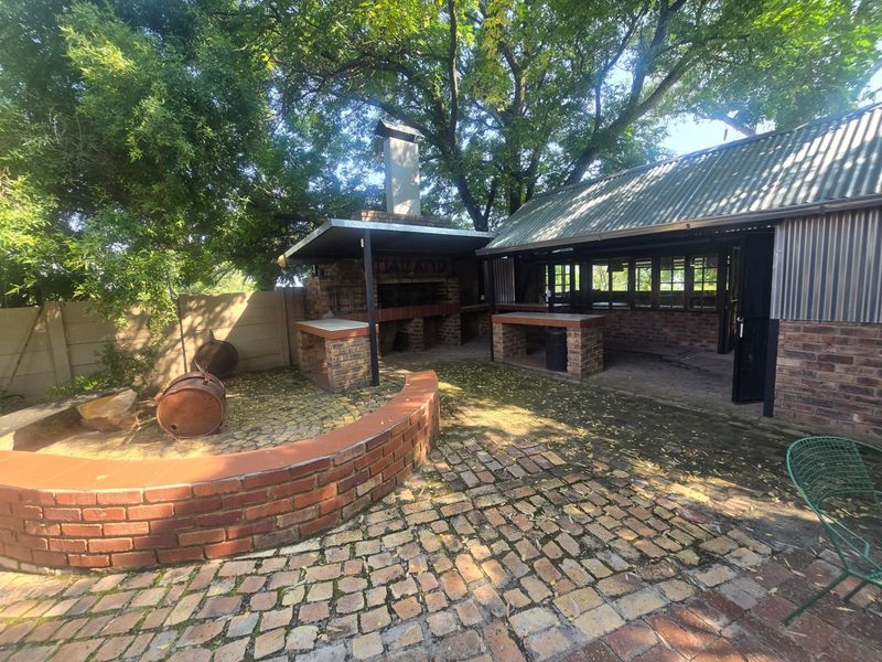 Outdoor entertainment area featuring a built-in brick braai, covered patio space, and brick paving, set within a mature garden environment.