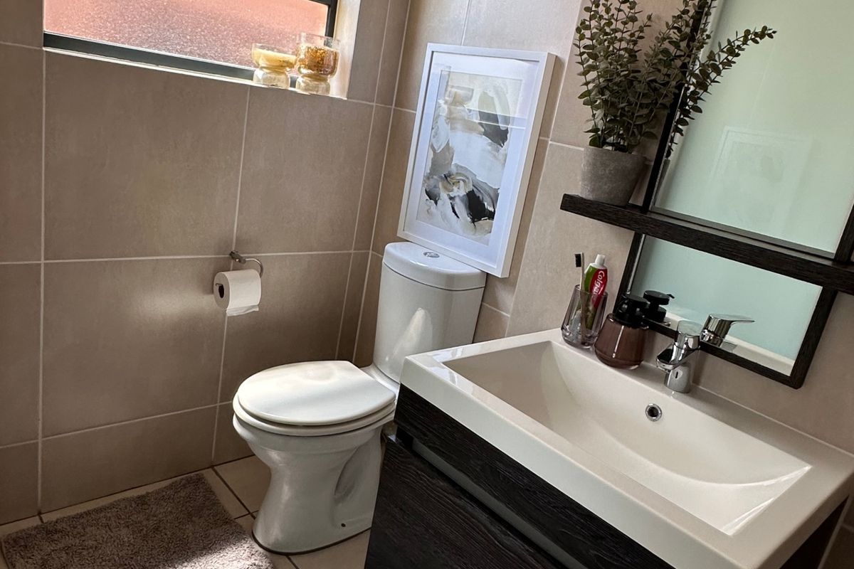 A modern bathroom featuring a wall-mounted vanity with a ceramic basin, tiled walls and flooring, and a functional top-hung window for natural light.