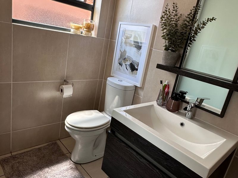 A modern bathroom featuring a wall-mounted vanity with a ceramic basin, tiled walls and flooring, and a functional top-hung window for natural light.