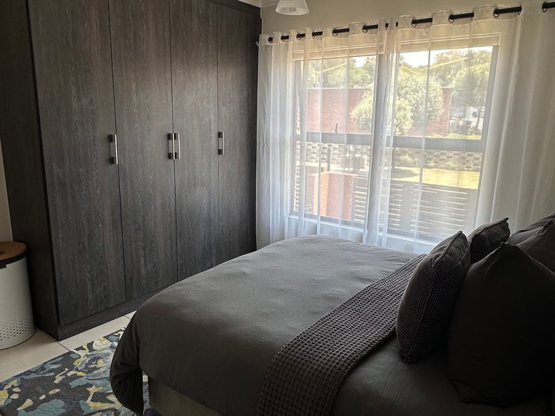 A well-maintained bedroom featuring dark wood built-in wardrobes, tiled flooring, and natural light through a window with sheer curtains.