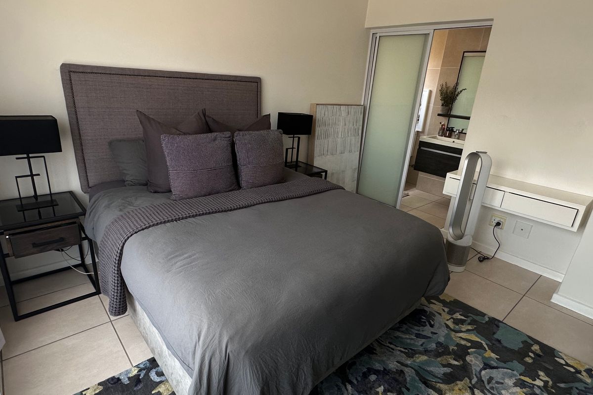 A well-maintained bedroom featuring tiled flooring and an adjoining en-suite bathroom accessed via a sliding door.