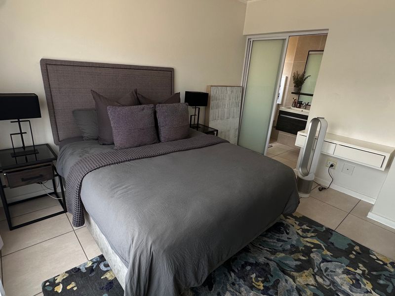 A well-maintained bedroom featuring tiled flooring and an adjoining en-suite bathroom accessed via a sliding door.