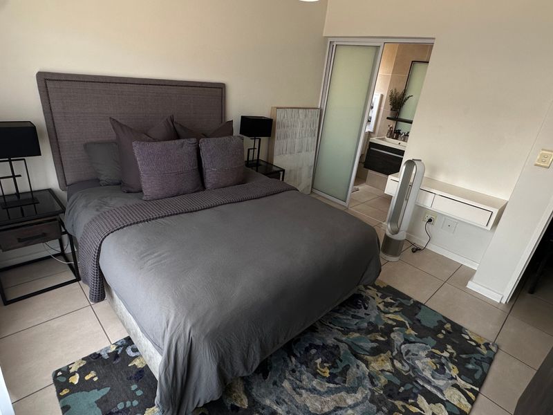 A well-maintained bedroom featuring tiled flooring, a built-in vanity, and direct access to an en-suite bathroom through a sliding door.