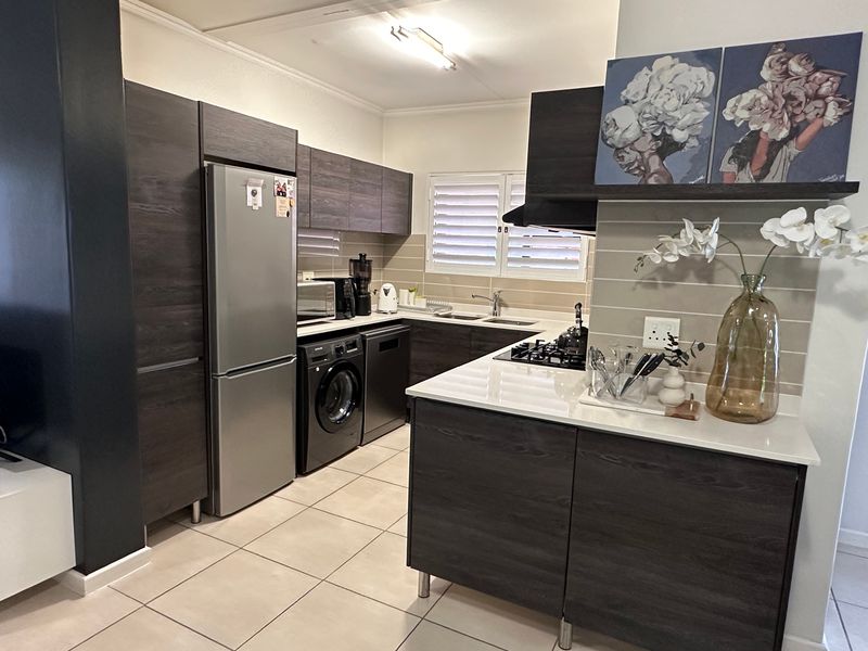 Modern kitchen featuring dark wood cabinetry, stone countertops, integrated gas hob, extractor fan, and tiled flooring with functional layout.