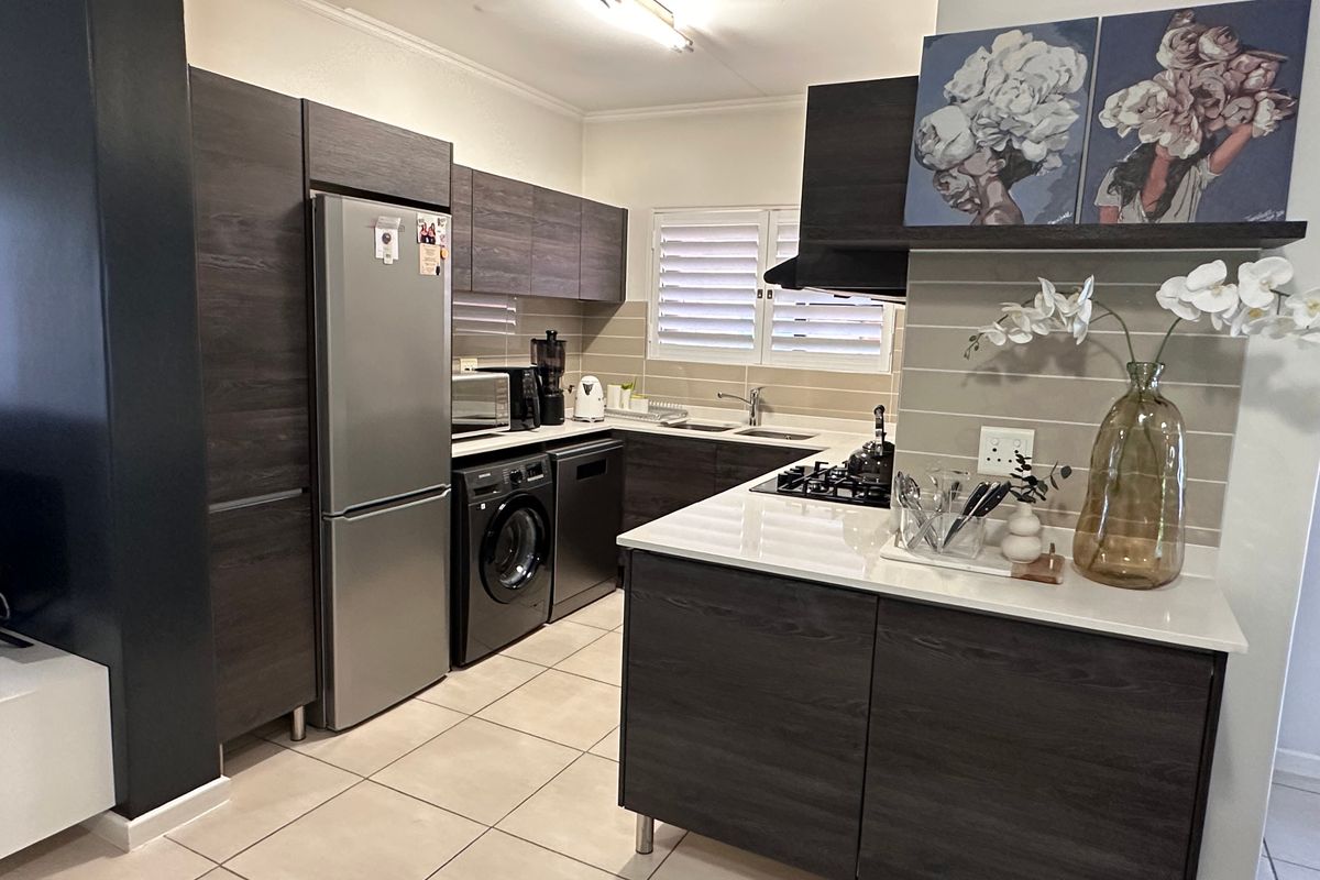 Modern kitchen featuring dark wood cabinetry, stone countertops, integrated gas hob, extractor fan, and tiled flooring with functional layout.