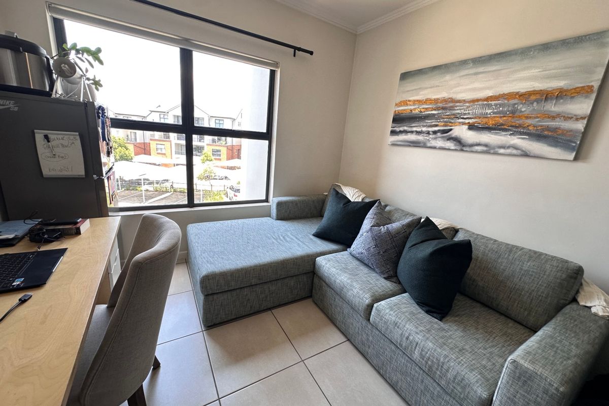 A well-lit living room featuring neutral tiled flooring and a large window providing natural light and an exterior view.