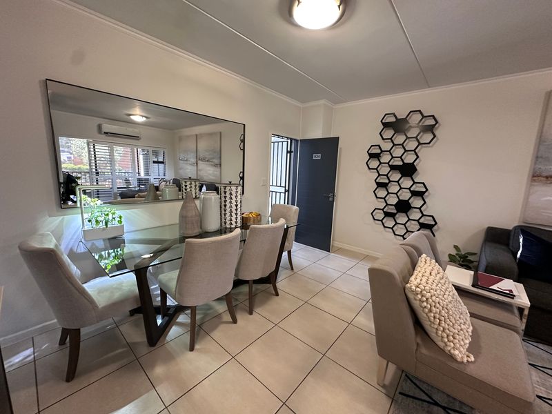A well-maintained dining area featuring neutral tiled flooring, a large wall-mounted mirror, and direct access to the apartment entrance.