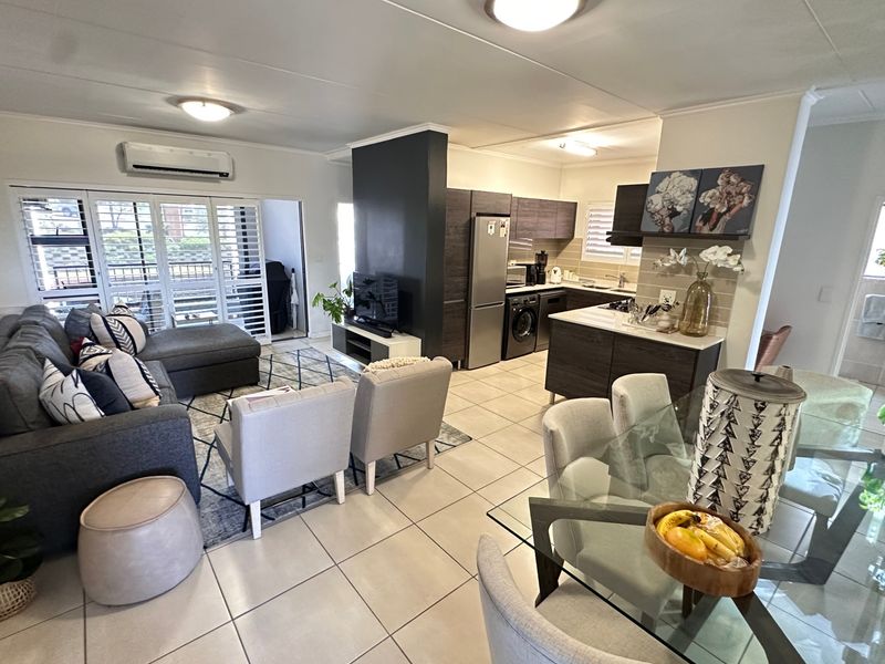 Spacious open-plan living and dining area featuring a modern kitchen with built-in cabinetry, tiled floors, and direct access to a private balcony.