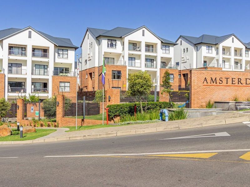 A clear street-level view of the Amsterdam apartment complex, showcasing its brick facade, multi-story residential blocks, and well-maintained landscaped grounds.