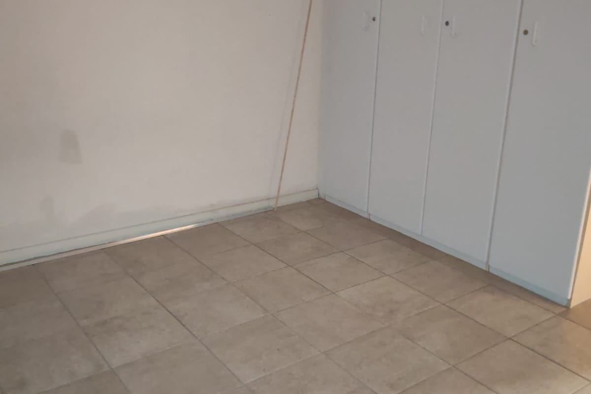 An empty bedroom featuring neutral tiled flooring and white built-in cupboards, providing a blank canvas for personalization.